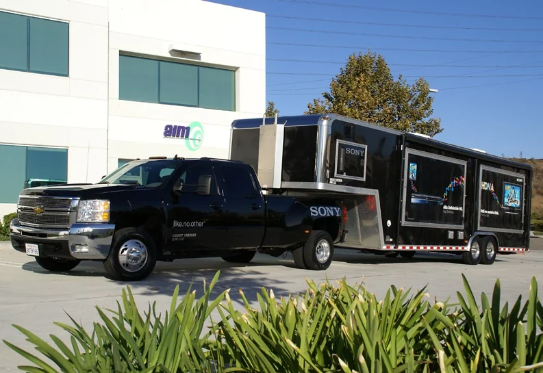 Sony truck and trailer parked outside a building displaying the AIM logo